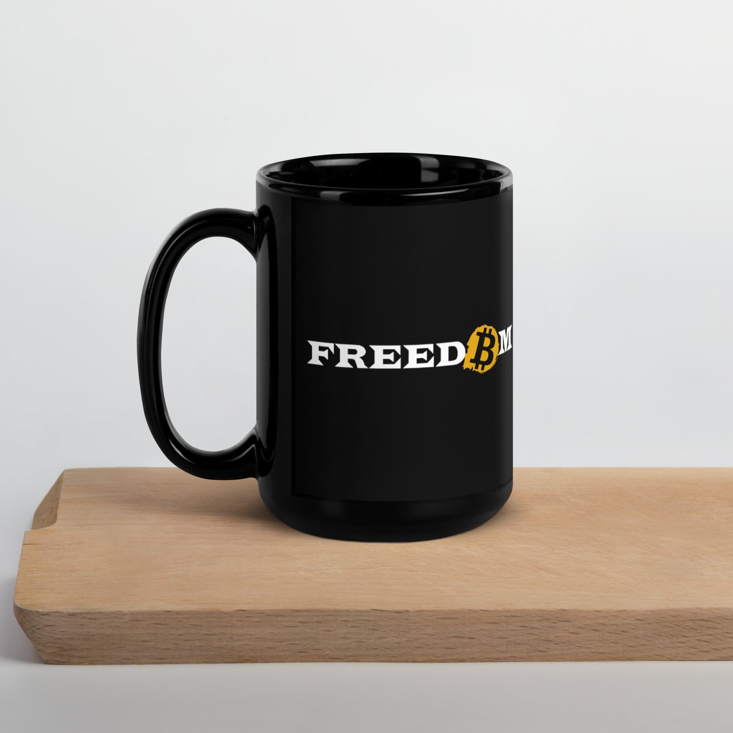 A 15oz black mug with the word ‘Freedom’ written on it on either side of it in white letters. The letter ‘o’ is replaced with the orange bitcoin logo. Side view.