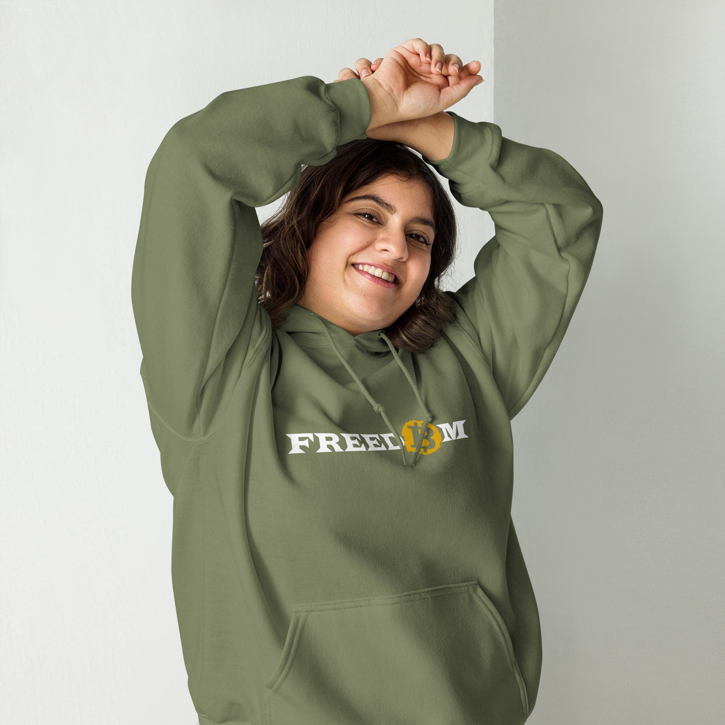 Female model wearing a military green color heavy blend hoodie with the word ‘Freedom’ written on it in white letters. The letter ‘o’ is replaced with the orange bitcoin logo.