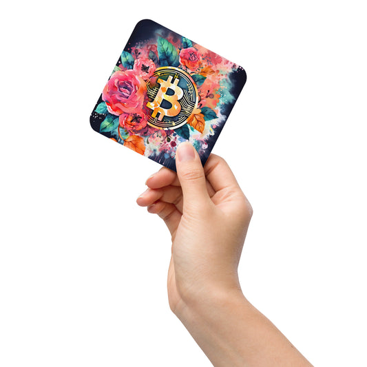 Female hand holding cork back coaster with floral bitcoin logo design on black background. 